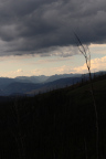 Photo of a landscape with dark hills in the foreground, gray mountains in the background and sky with dark gray clouds 
